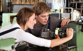 A cutting machine operator explains a work tool to a trainee